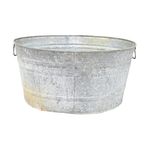 Puede incluir: Una tina de lavado grande y ovalada de metal galvanizado con un acabado gris plateado desgastado. El recipiente cuenta con un borde reforzado, detalles acanalados horizontales en las paredes exteriores y dos pequeñas asas de metal.