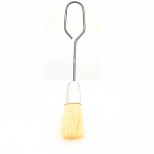 Puede incluir: Un pequeño cepillo plateado con un mango de alambre y una cabeza de cepillo de cerdas naturales. El cepillo está diseñado para limpiar y aplicar líquidos.