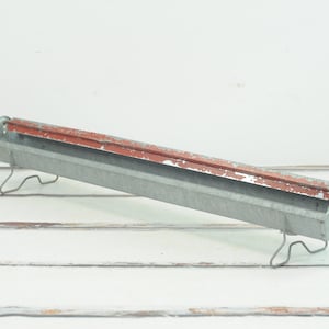 May include: A vintage metal chicken feeder with a red painted interior and wire legs. The feeder is made of galvanized metal and has a rustic look.