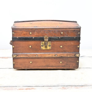 May include: A vintage wooden trunk with a curved top, brass hardware, and black metal bands. The trunk is brown with brass studs and a brass lock. The trunk is a storage container.
