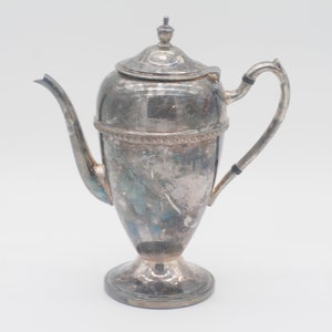 May include: A silver teapot with a rounded body and a decorative handle. The teapot has a tarnished finish and a detailed design.