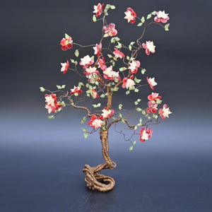 May include: A decorative bonsai tree sculpture with a twisted trunk and delicate branches. The tree features red and white flowers with green leaves, set against a dark background. The sculpture is an artistic representation of nature.