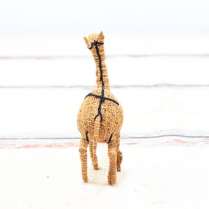 May include: A brown woven giraffe figurine with black string accents. The giraffe is standing on a white surface.