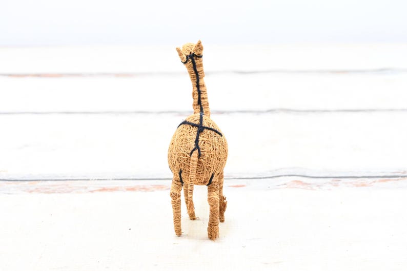 May include: A brown woven giraffe figurine with black string accents. The giraffe is standing on a white surface.