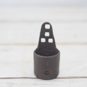 May include: A dark brown metal ring with a cutout design and a small circle on the bottom. The ring is made of a textured metal and has a rustic look.