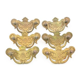 May include: Six antique brass drawer pulls with a floral design. Each pull has a decorative backplate with a central flower and curved handles. The pulls are arranged in two rows of three against a white background.