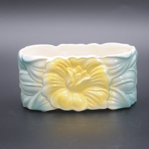 May include: A ceramic planter with a yellow flower design. The planter is oval shaped and has a light blue and white glaze.