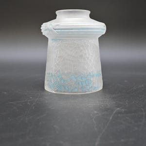 May include: A frosted glass lampshade with a unique design. The lampshade has a cylindrical shape with a flared base and a decorative top. It features a cracked glass pattern with blue accents, adding a touch of color and visual interest.