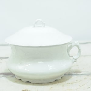 May include: A white porcelain chamber pot with a lid and a handle. The pot features a floral design.