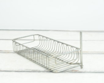 May include: A silver wire rack with a rectangular shape and a curved front edge. The rack is designed for storage or display.