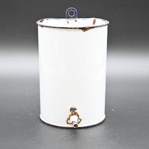 May include: White enamelware pitcher with a blue rim and a spout. The pitcher has a handle on the top and is slightly rusted.