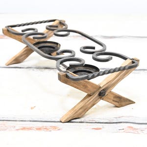 Puede incluir: Un portavelas rústico de madera y metal con un diseño decorativo enrollado. El portavelas tiene cuatro patas y puede contener varias velas.