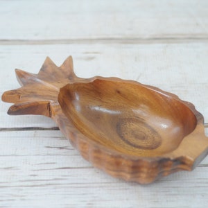 May include: A wooden pineapple-shaped bowl, carved from a single piece of wood. The bowl is empty and has a natural wood finish.