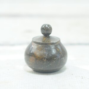 Op de afbeelding: Een kleine, donkerbruine houten pot met een rond deksel. De pot heeft een gladde, gepolijste afwerking.