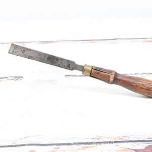May include: A vintage wood chisel. It features a metal blade and a wooden handle, with a brass ferrule. The chisel is designed for woodworking. The tool is set against a white background.