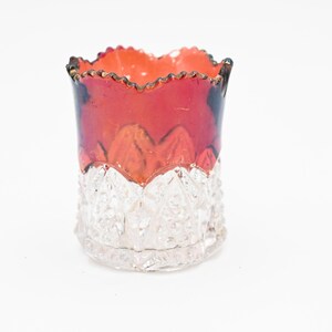 Op de afbeelding: Een kleine, heldere glazen tandenstokerhouder met een rode en zwarte glazen bovenkant. De houder heeft een getextureerd, diamantvormig patroon.