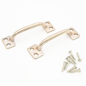 Puede incluir: Dos tiradores de cajón de metal plateado de estilo vintage con un diseño de asa curvada. Cada tirador tiene una base rectangular con cuatro orificios para tornillos. También se incluye un pequeño montón de tornillos plateados.