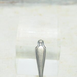 May include: Close-up of the top of a silver spoon with an ornate design and the letter "T" engraved on the handle.