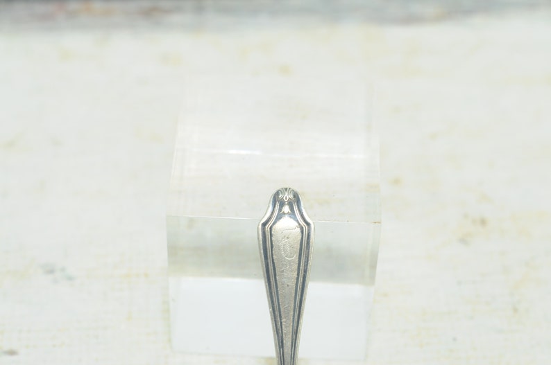 May include: Close-up of the top of a silver spoon with an ornate design and the letter "T" engraved on the handle.