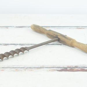 May include: A vintage wooden handled drill bit with a metal twist drill bit. The drill bit is rusty and has a wooden handle.