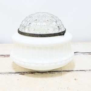 May include: A vintage white glass light fixture with a decorative, ribbed base and a clear, faceted glass dome. The dome is held in place by a dark metal band. The fixture is likely an antique ceiling light.