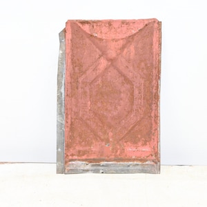 May include: A weathered, rectangular metal panel with a faded, reddish-brown finish. The panel features embossed geometric patterns, including a central hexagon and a curved top. The edges are bordered by a silver metal frame.