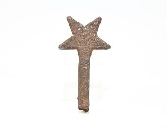 May include: A rustic, weathered metal object shaped like a five-pointed star attached to a vertical rectangular stem. The surface has a dark, oxidised brown texture with visible pitting. The letters "HMC" are embossed vertically on the stem.