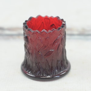 Op de afbeelding: Een kleine, rode glazen vaas met een boomschorsontwerp. De vaas is ongeveer 7,5 cm hoog en heeft een brede opening.