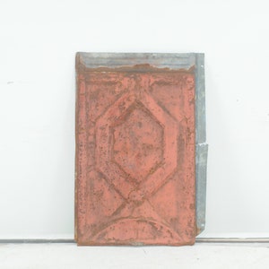 May include: A vintage metal ceiling tile with a geometric design. The tile is painted a rusty orange colour and has a silver border.