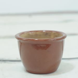 Op de afbeelding: Een kleine, terracottakleurige keramische pot met een ronde vorm. De pot is leeg en heeft een gladde, geglazuurde afwerking.