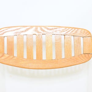 May include: Close-up of a vintage chair back. The backrest is made of light-colored wood slats and a curved wooden frame. The chair has shiny, silver metal legs. The design is minimalist and mid-century modern.