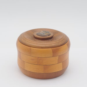 May include: A wooden box with a lid, made of light and dark wood, with a small round stone inlay in the center of the lid.