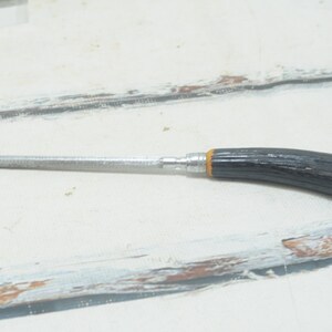 May include: A silver metal file with a black and yellow wooden handle. The file is about 6 inches long.