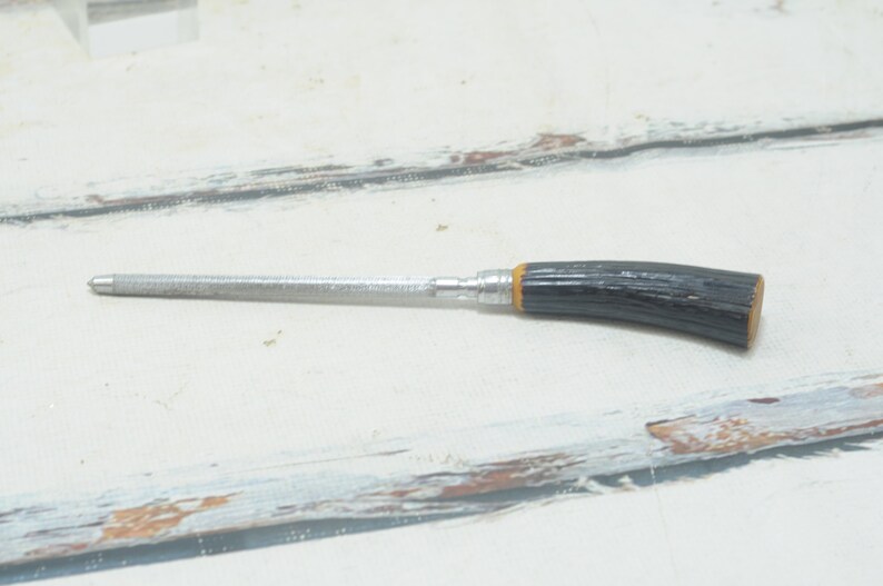 May include: A silver metal file with a black and yellow wooden handle. The file is about 6 inches long.