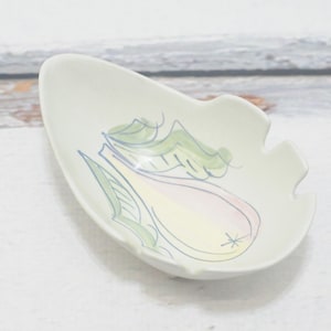 Puede incluir: Un plato de cerámica blanca con forma de pera con un diseño pintado en verde y azul. La pera tiene un rubor rosado en un lado.