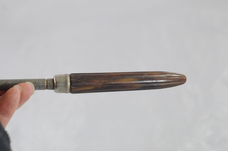 May include: A vintage metal and wood screwdriver with a brown wooden handle. The handle has a ribbed design and a silver metal cap.