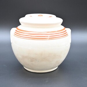May include: White ceramic jar with a lid and brown stripes around the middle. The jar has two small handles on the sides.