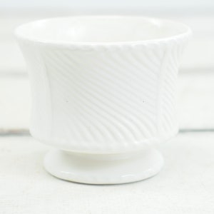 Op de afbeelding: Witte keramische plantenpot met een swirl-ontwerp. De pot heeft een brede basis en een smalle opening.