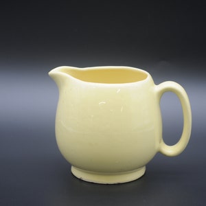 May include: A pale yellow ceramic jug with a rounded body and a handle. The jug is sitting on a black surface.