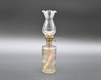May include: A clear glass oil lamp with a gold-coloured design on the base and a clear glass chimney.
