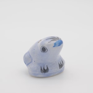 May include: A small blue ceramic rabbit figurine with black and white painted details. The rabbit has a blue and white painted nose and black eyes.