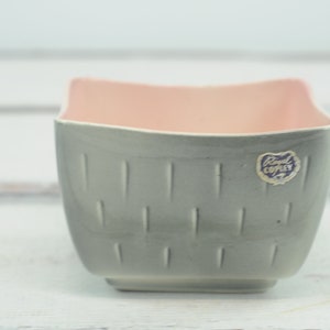 Puede incluir: Un macetero de cerámica gris con interior rosa y una etiqueta "Royal Copley". El macetero tiene un diseño texturizado y acanalado.