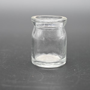 May include: A clear glass bottle with a rounded bottom and a wide mouth. The bottle is empty and has a slightly textured surface.