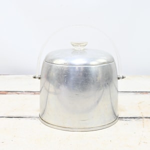 May include: A vintage silver ice bucket with a clear plastic handle and lid. The bucket has a rounded shape with a lid and a small, clear knob on top. The handle is arched, and the bucket has a shiny, metallic finish.