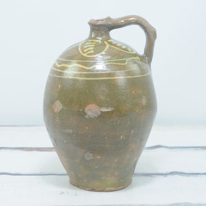 May include: A green ceramic pitcher with a handle and yellow painted designs. The pitcher has a rustic, vintage look.