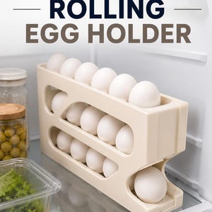 Może przedstawiać: Beżowy plastikowy stojak na jajka z kilkoma poziomami, zawierający kilka białych jaj. Napis ROLLING EGG HOLDER jest wydrukowany w kolorze ciemnoniebieskim i brązowym u góry. Konstrukcja posiada nachylone szczeliny do dozowania jajek.