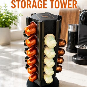 以下が含まれることがあります： 上部に「COFFEE CAPSULE STORAGE TOWER」の文字が記された黒い六角形のコーヒーカプセル収納タワー。タワーにはオレンジ色とライトグリーンのコーヒーカプセルを保持する垂直スロットがあり、上面にはネスプレッソのロゴが配置されています。