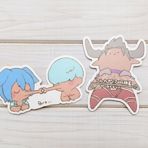 Puede incluir: Tres pegatinas de dibujos animados sobre una superficie de vetas de madera clara. Una pegatina muestra dos figuras tocándose la nariz con la palabra "Bro..." debajo. La otra pegatina presenta una figura con cuernos con texto japonés.