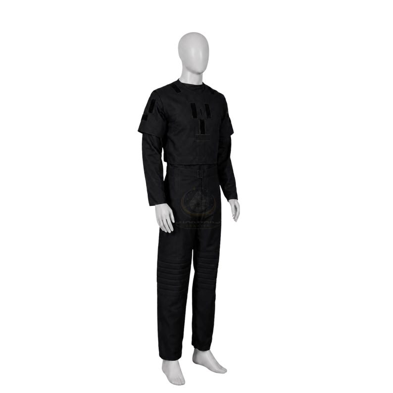 Pode incluir: Um conjunto de uniforme preto de duas pe&ccedil;as composto por uma blusa de manga curta com remendos retangulares no peito e ombros, e cal&ccedil;as compridas a condizer com detalhes de acolchoamento horizontal na zona das coxas, num manequim.
