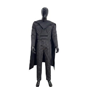 May include: A black costume set on a mannequin, featuring a long-sleeved top with geometric patterns on the sleeves, a matching pair of trousers with visible white stitching, and a long cape draped over the shoulders, all in a dark charcoal black.